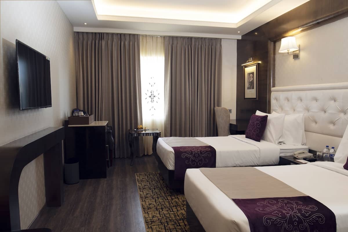 A hotel room with two beds, a desk, a flat-screen TV, and a window with curtains.