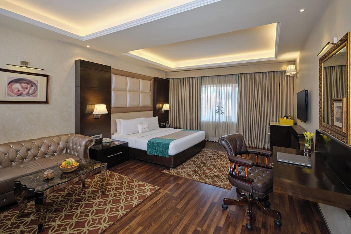 A hotel room with a large bed, a sofa, a desk, and a television.