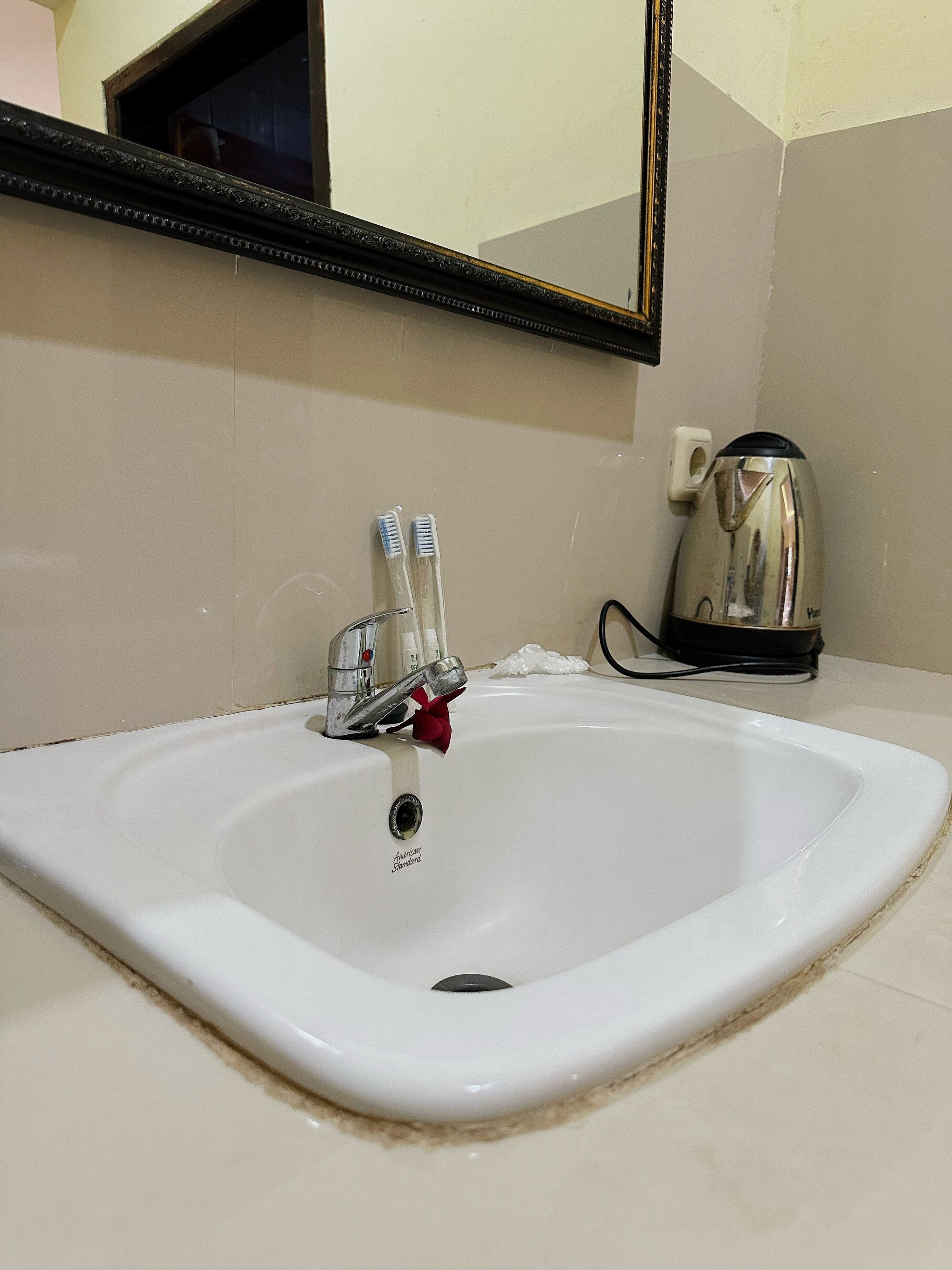Un lavabo con grifo, dos cepillos de dientes y una tetera.