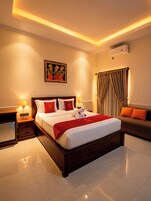 Habitación de hotel con una cama grande, mesitas de noche, un sofá, un cuadro en la pared y un equipo de aire acondicionado.