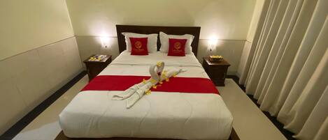 A hotel room with a large bed, two bedside tables, a nightstand, a red throw blanket, a decorative swan, and a painting on the wall.