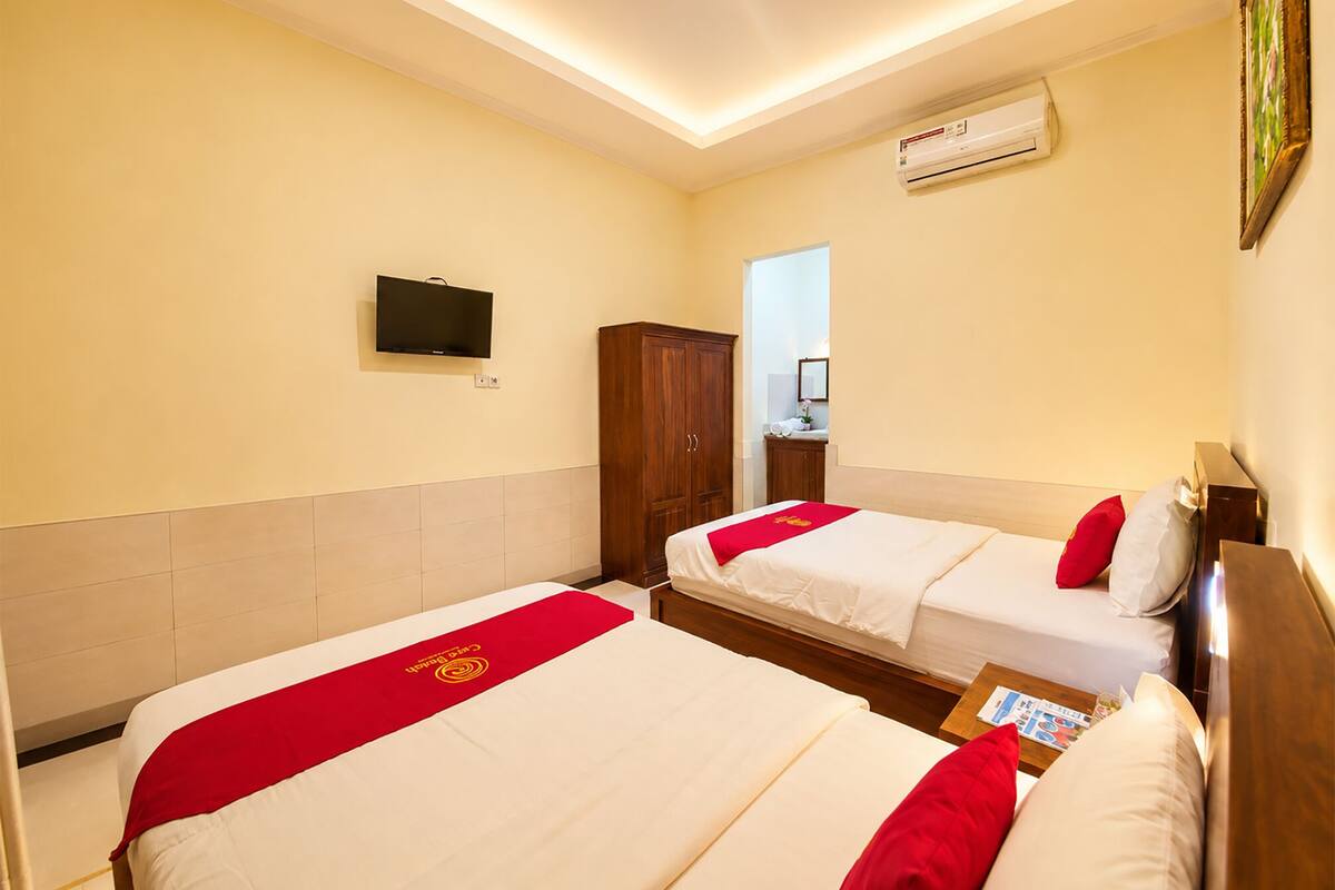 A hotel room with two beds, a TV, an air conditioner, a wardrobe, and a mirror.