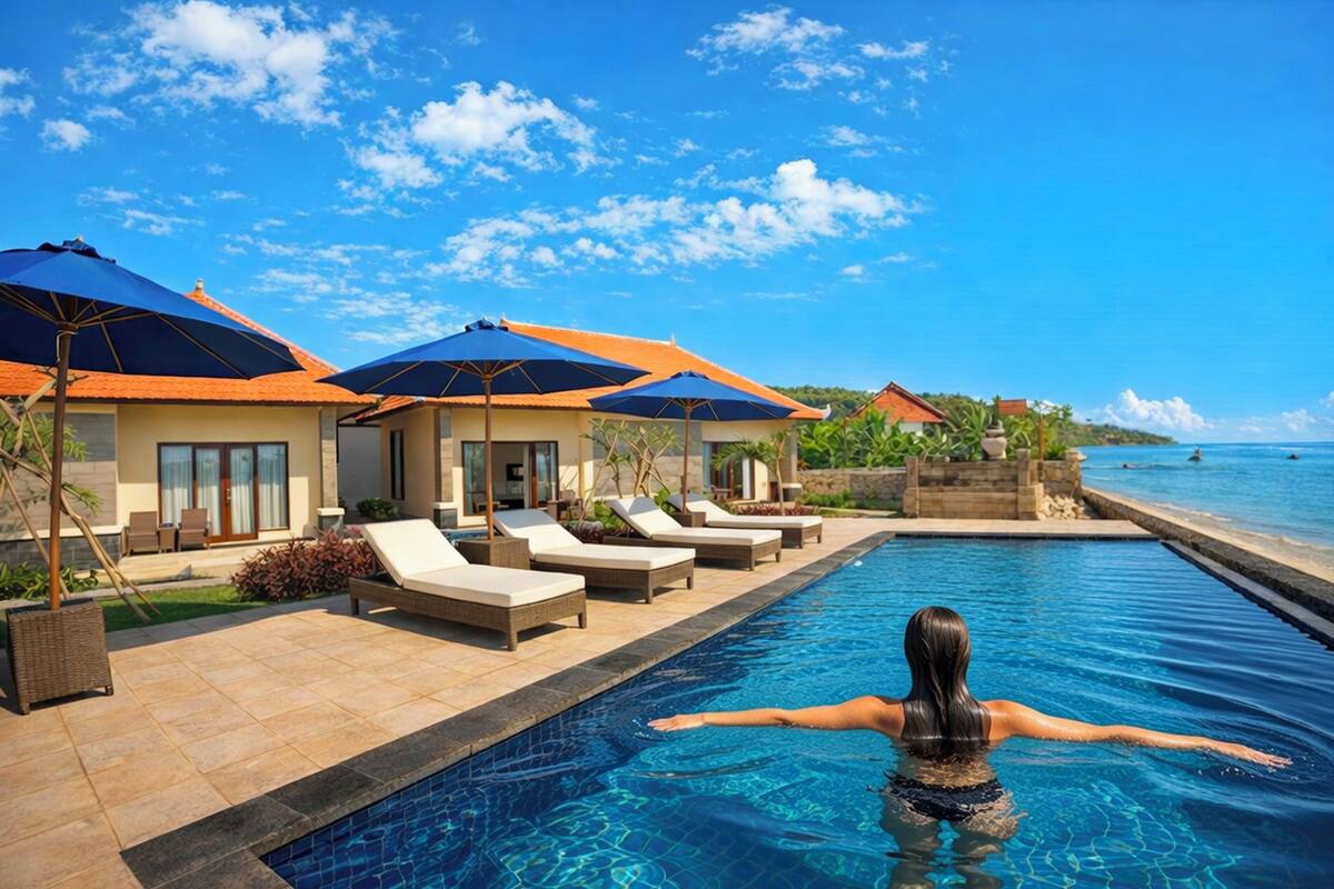 A swimming pool with lounge chairs and umbrellas, a clear sky, and a view of the sea.