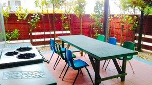 Un patio exterior con una mesa y sillas, una estufa de gas y una cerca roja al fondo.