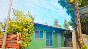 Un pequeño edificio de una sola planta con fachada verde y tejado azul. Un cartel de madera con caracteres chinos está a la izquierda del edificio.