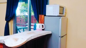 Una cocina con un microondas encima de un refrigerador, una tetera en la encimera y una ventana con cortinas.