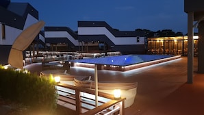 Un área de piscina al aire libre con sillones de descanso y una zona de estar cubierta, rodeada de edificios modernos.