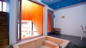 Un interior moderno con una bañera de madera, una zona de comedor y vistas a través de un amplio ventanal.