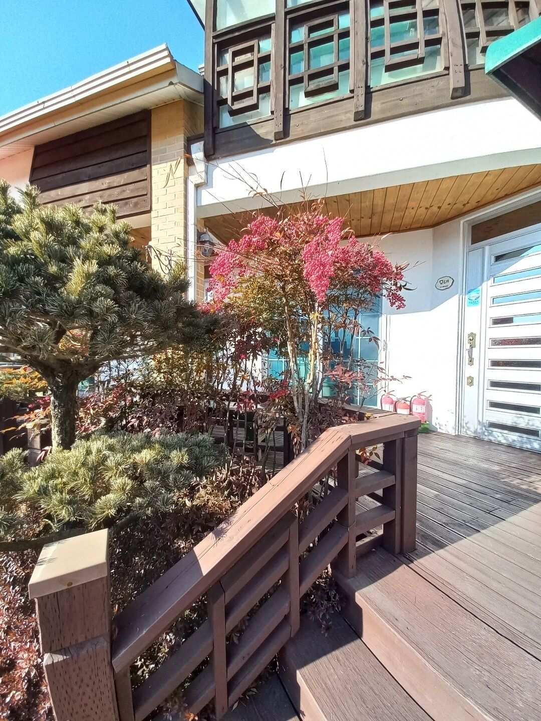A wooden deck with a railing, a small tree with pink flowers, and a building with a garage door.