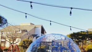 A transparent dome structure with a table and chairs inside, surrounded by a grassy area with patterned ground. - Gyeongju Orsay Pension (Gyeongju)