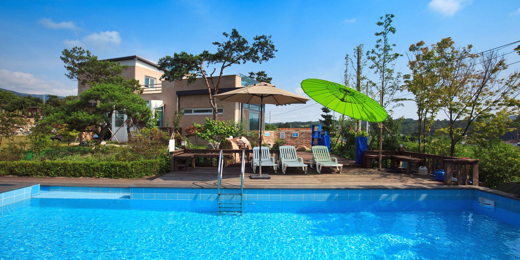 Une piscine avec une terrasse en bois, des chaises longues et un parasol vert.