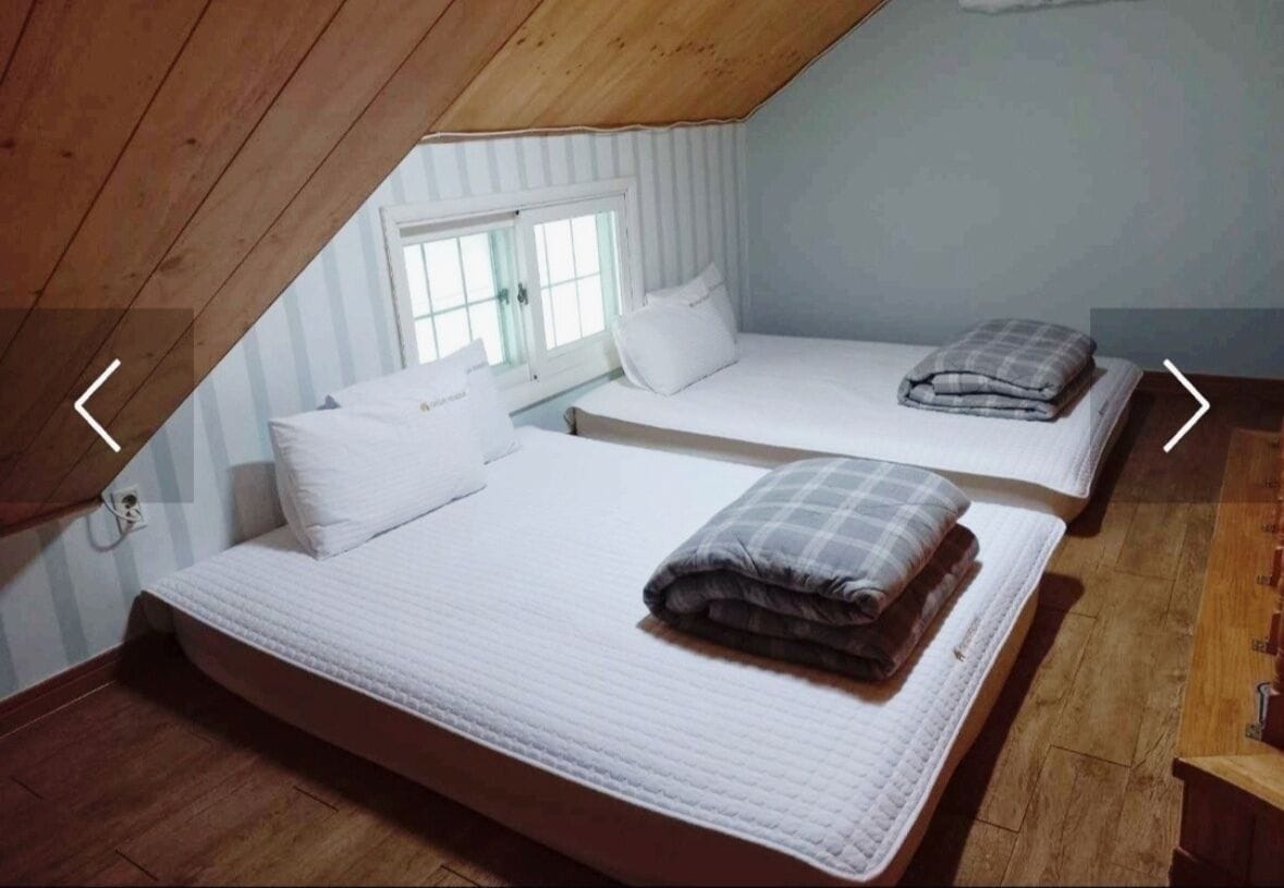 Een knus slaapkamer op zolder met twee bedden, houten balken en een raam.