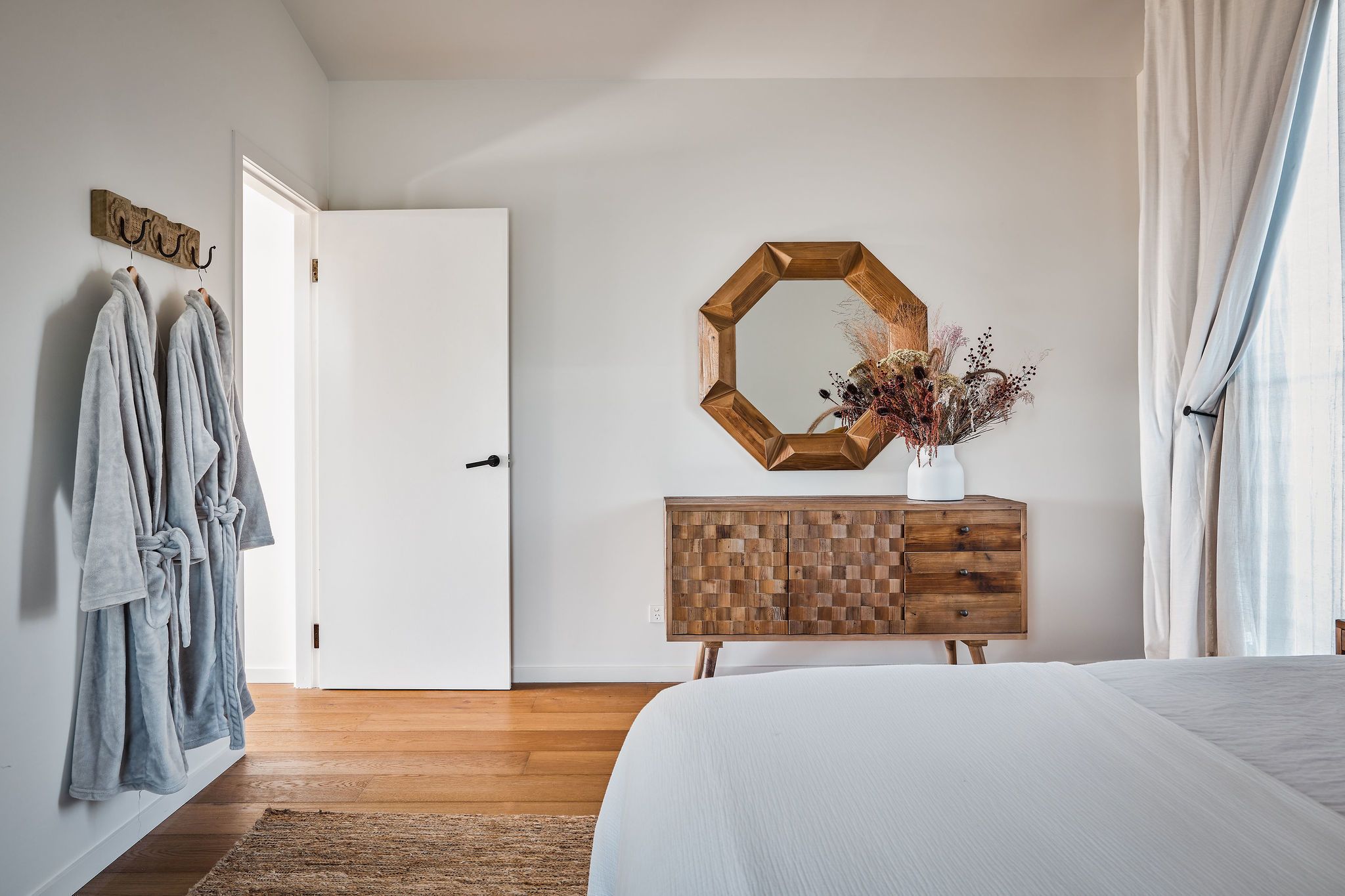 A bedroom with a wooden dresser, a large mirror, and a bed.