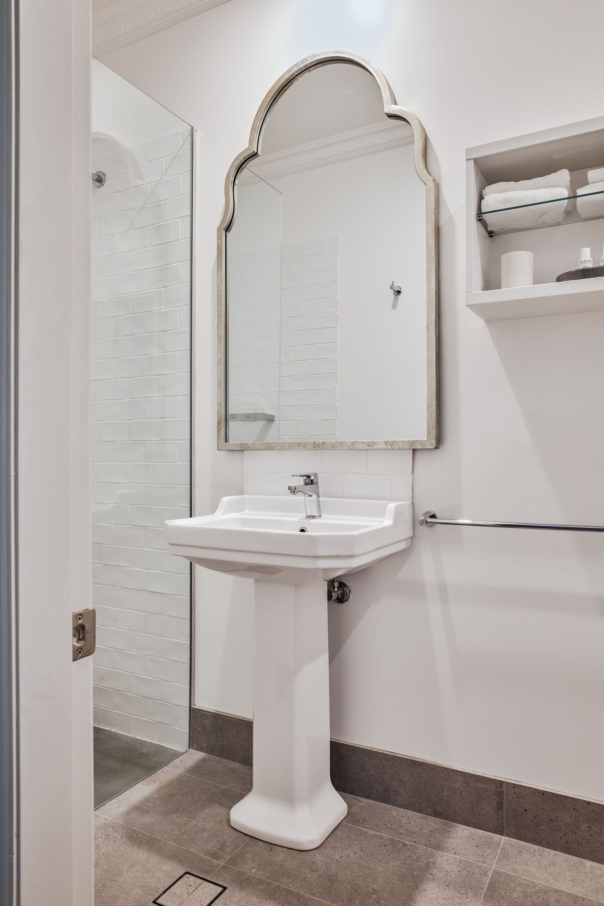 A bathroom with a white pedestal sink, a mirror with an ornate frame, and a towel rack with folded towels.