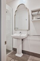 A bathroom with a white pedestal sink, a mirror with an ornate frame, and a towel rack with folded towels.