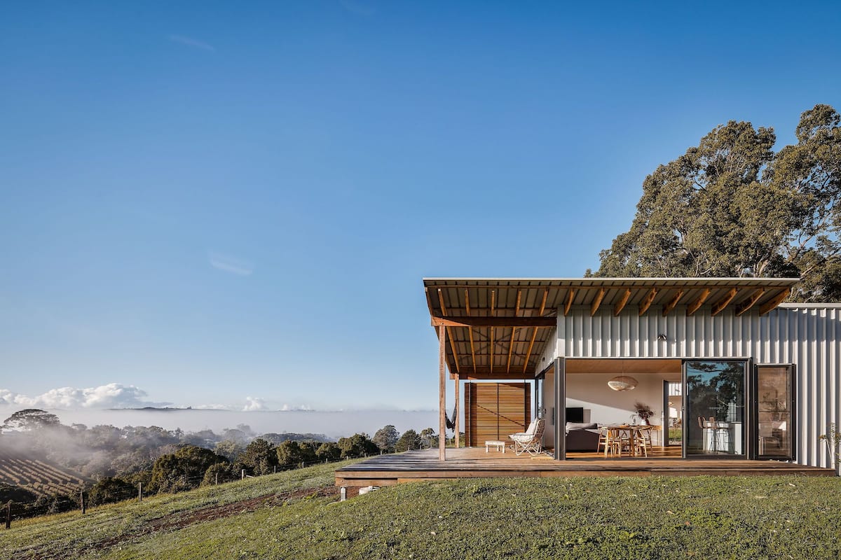 Ein modernes Haus mit einer großen Terrasse, einem Essbereich und Blick auf die Landschaft.