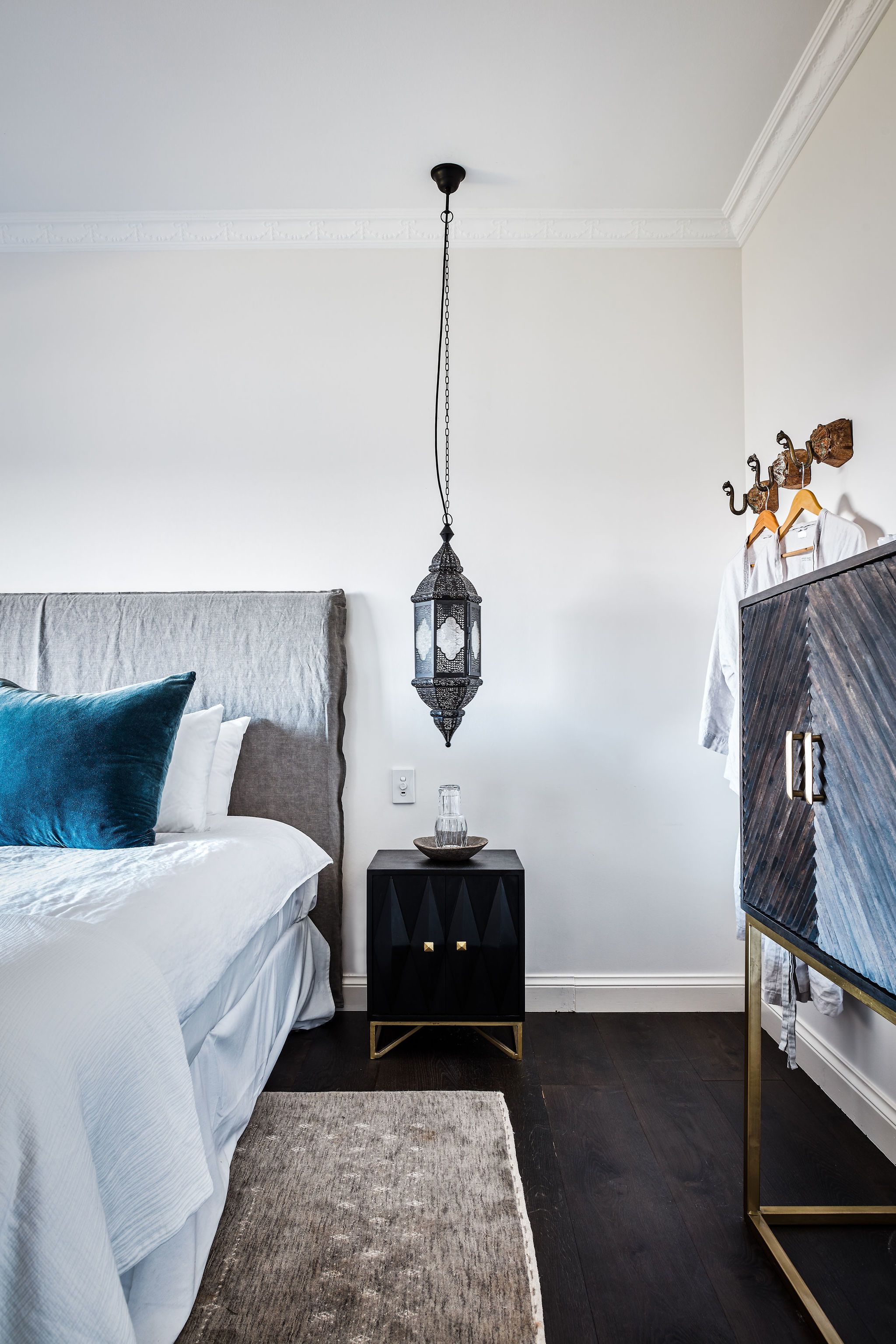 A bedroom with a bed, a nightstand, a wardrobe, and a hanging lantern.