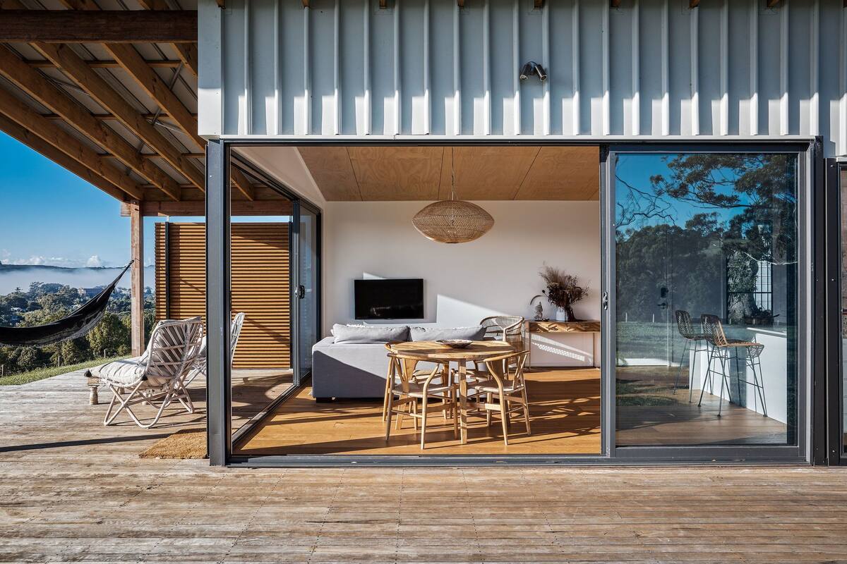 Ein modernes Haus mit einer großen Schiebetür, die auf eine Terrasse mit Sofa, Tisch und Stühlen führt.