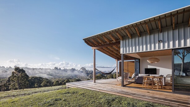 A modern house with a wooden deck, a hammock, and a TV in a large window. - 99 Acres Bangalow Retreat (Bangalow)
