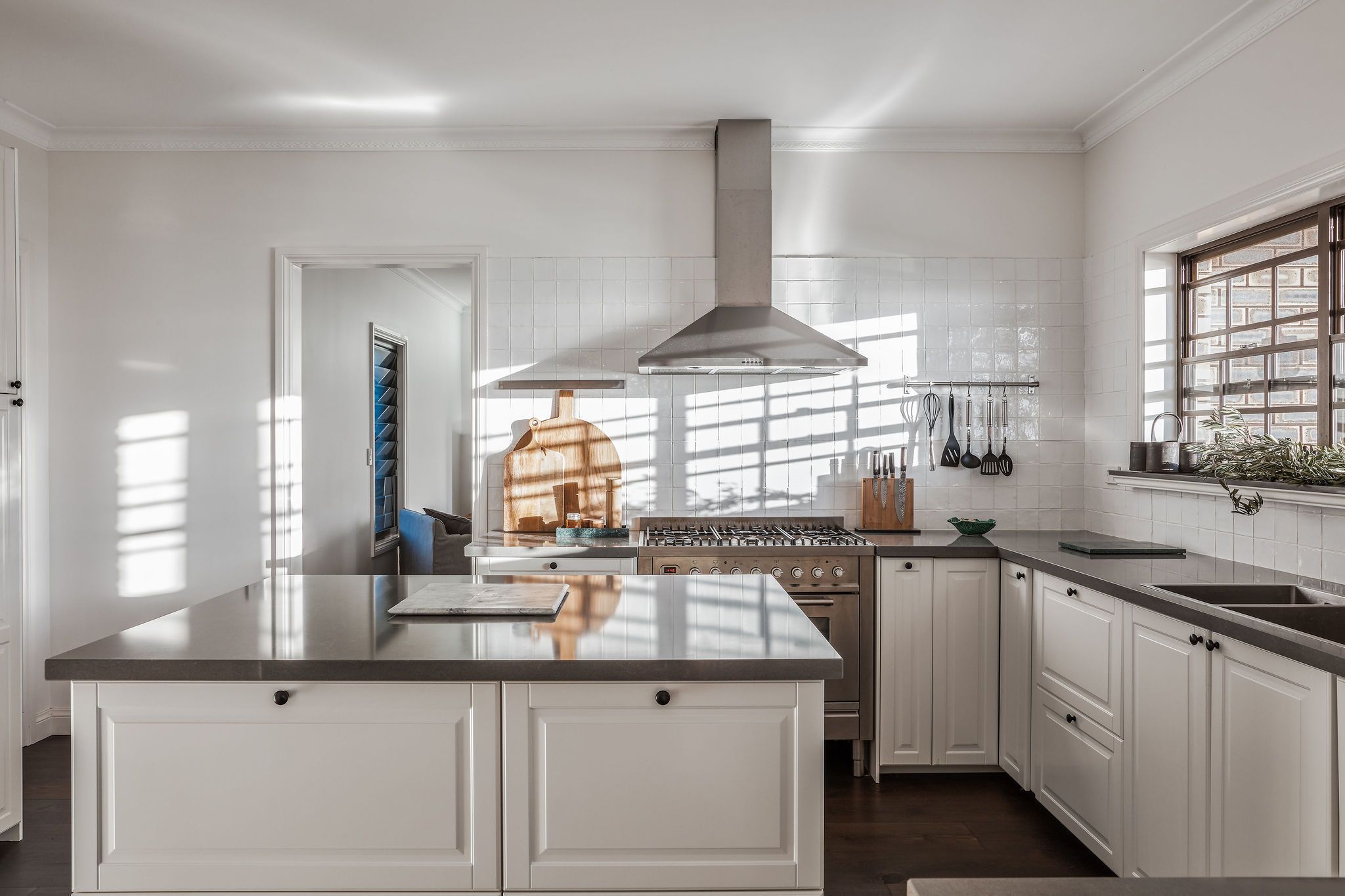 Una cocina moderna con armarios blancos, una isla grande, electrodomésticos de acero inoxidable y un ventanal que proporciona luz natural.