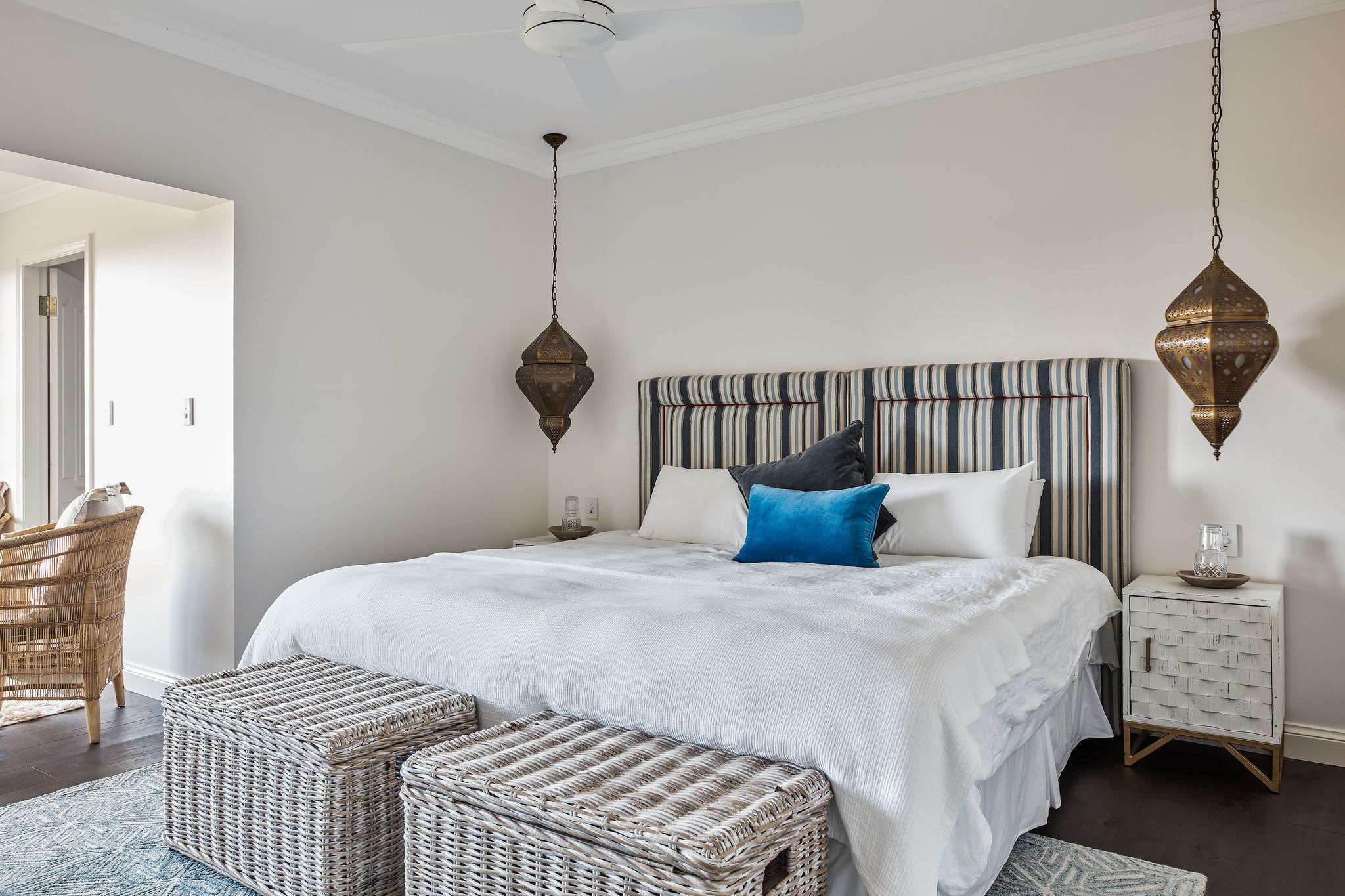 A bedroom with a large bed, a striped headboard, wicker furniture, and a hanging light fixture.
