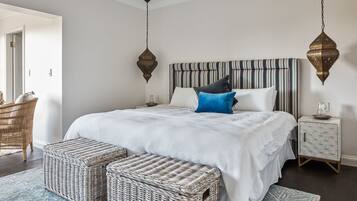 A bedroom with a large bed, a striped headboard, wicker furniture, and a hanging light fixture.