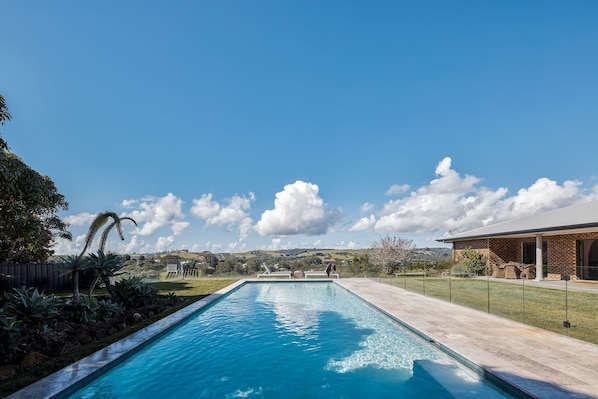 Ein rechteckiger Pool mit glasklarer, blauer Wasserfläche, umgeben von einer gepflasterten Terrasse.