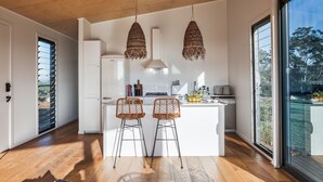 A modern kitchen with two bar stools, a large window, and a view of the outdoors. - 99 Acres Bangalow Retreat (Bangalow)