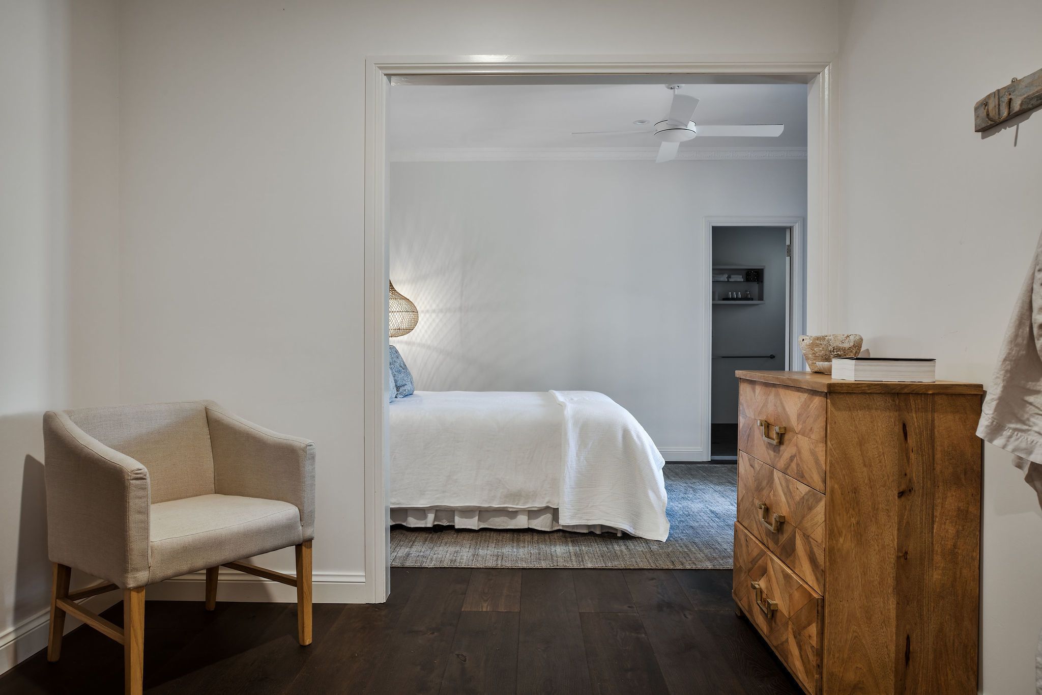 Ein Schlafzimmer mit einem Bett, einem Sessel, einer Holzkommode und einem Deckenventilator.