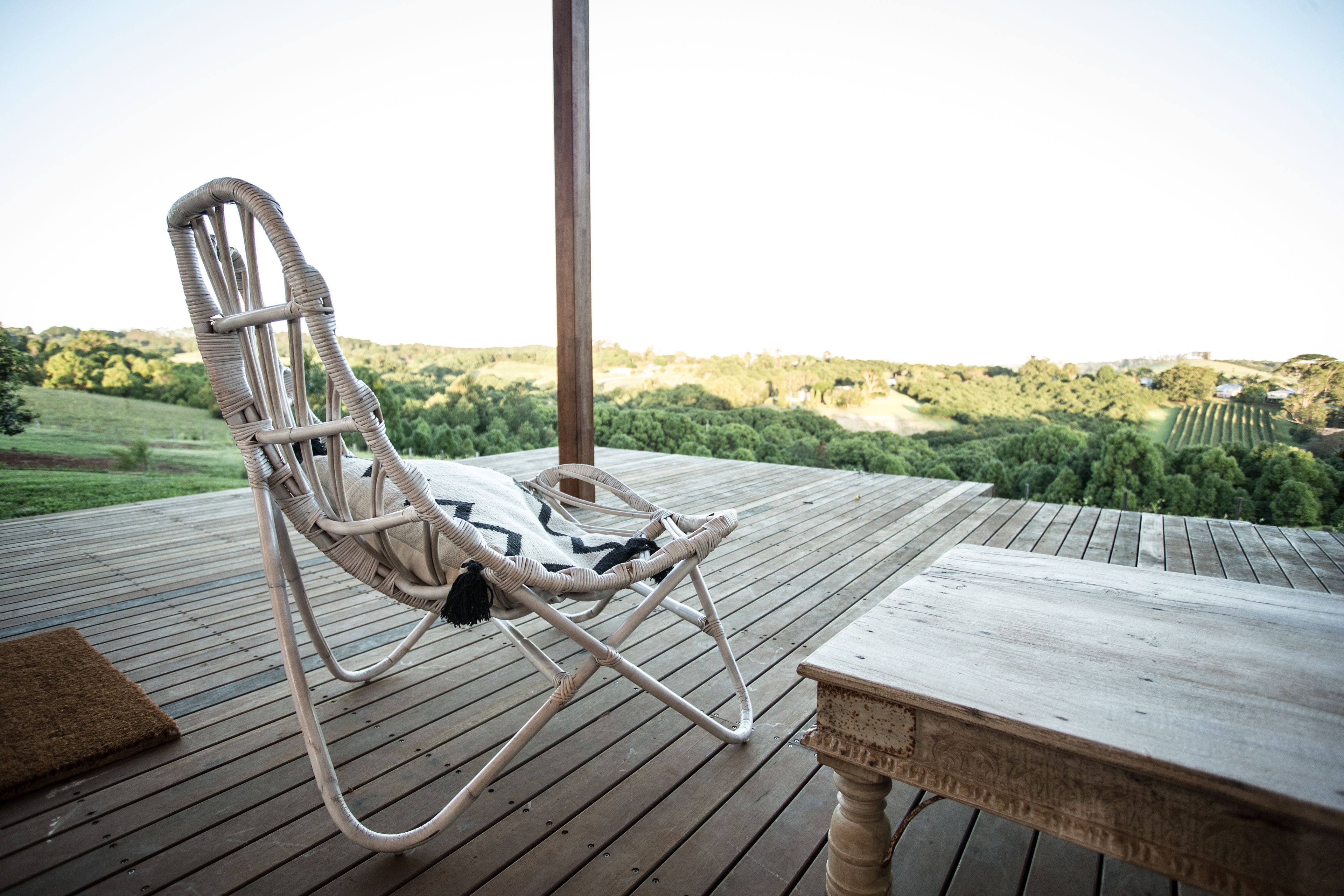 Una silla de mimbre sobre una terraza de madera, con vista a un paisaje verde.
