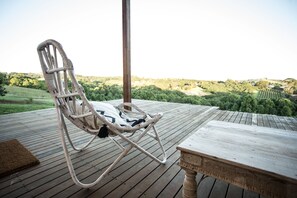 Ein Korbstuhl auf einer Holzterrasse mit Blick auf eine grüne Landschaft.