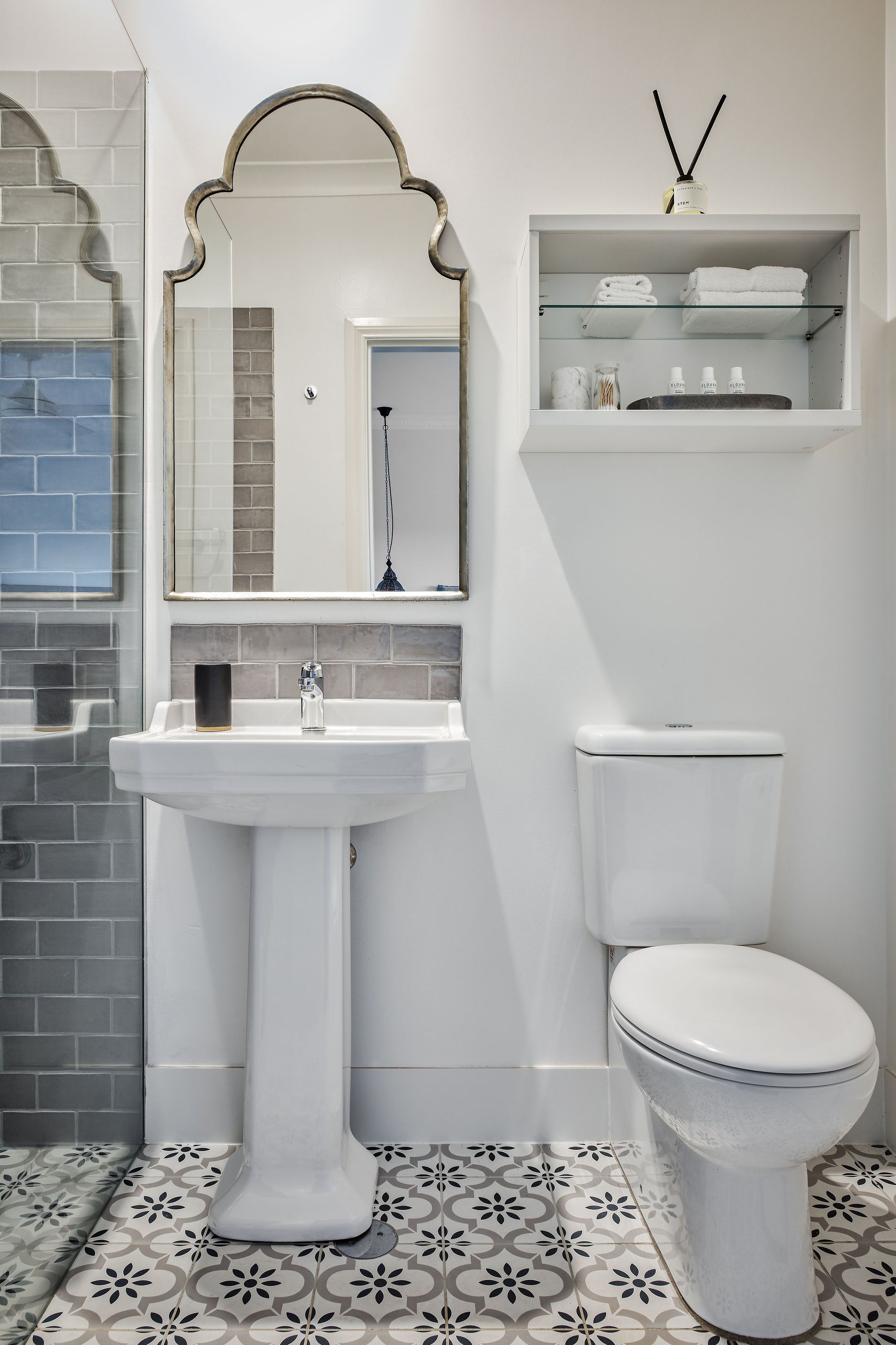 A bathroom with a pedestal sink, a toilet, and a shelf above the toilet.