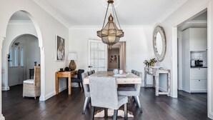 A dining area with a wooden table, grey upholstered chairs, and a hanging chandelier. - 99 Acres Bangalow Retreat (Bangalow)