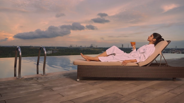 Una persona descansando en una tumbona junto a una piscina con vista a un paisaje urbano.