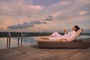 A person relaxing on a lounge chair by a pool with a cityscape view.