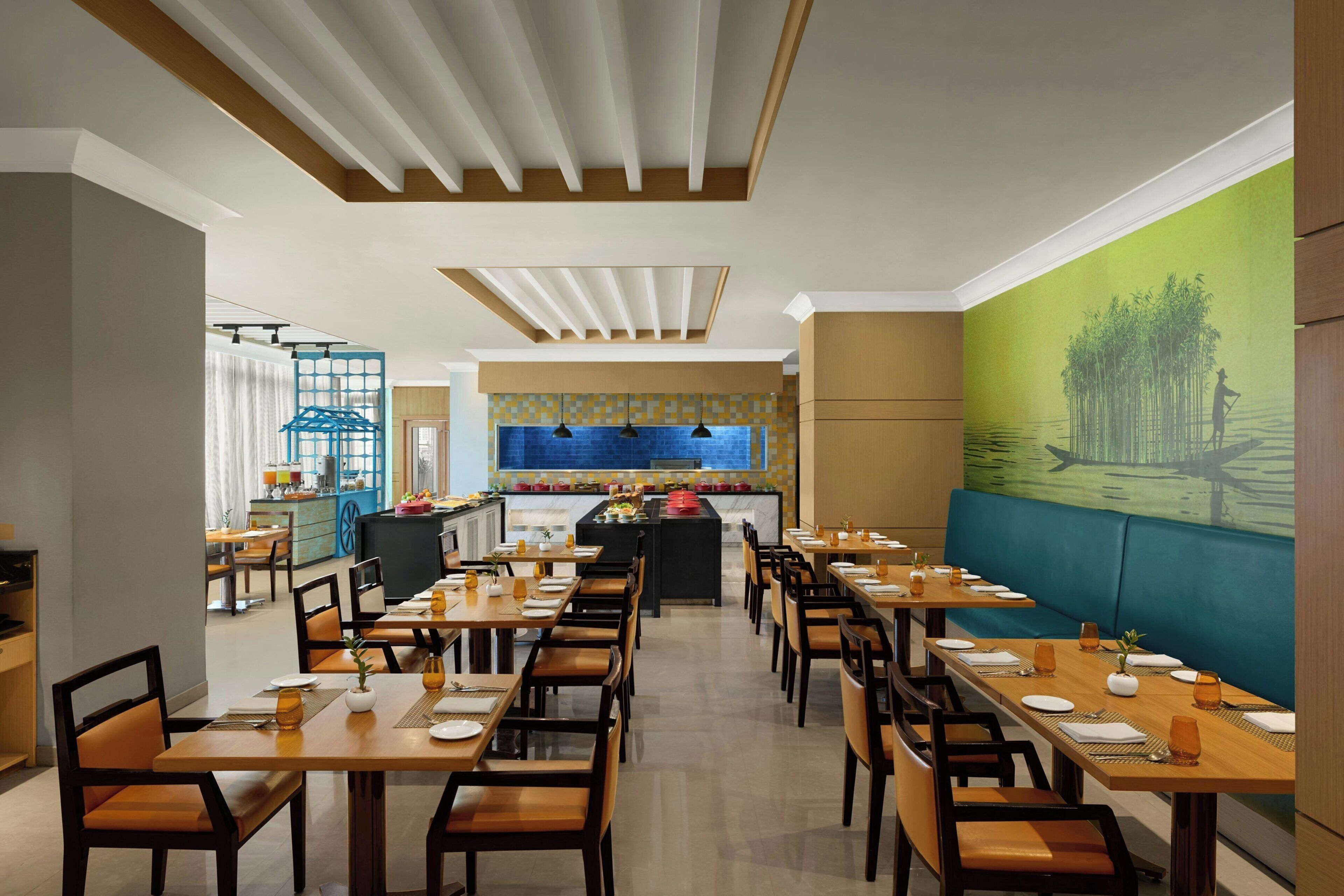 A restaurant with multiple dining tables and chairs, a kitchen area, and a mural on the wall.