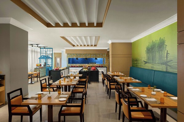 Un restaurante con varias mesas y sillas, una zona de cocina y un mural en la pared.