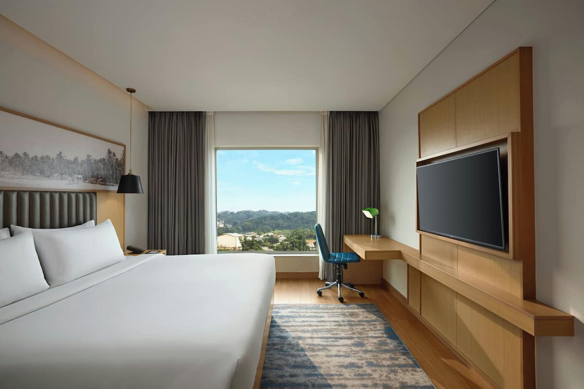 Une chambre d’hôtel avec un grand lit, un bureau avec une télévision, une chaise et une vue sur le paysage par la fenêtre.