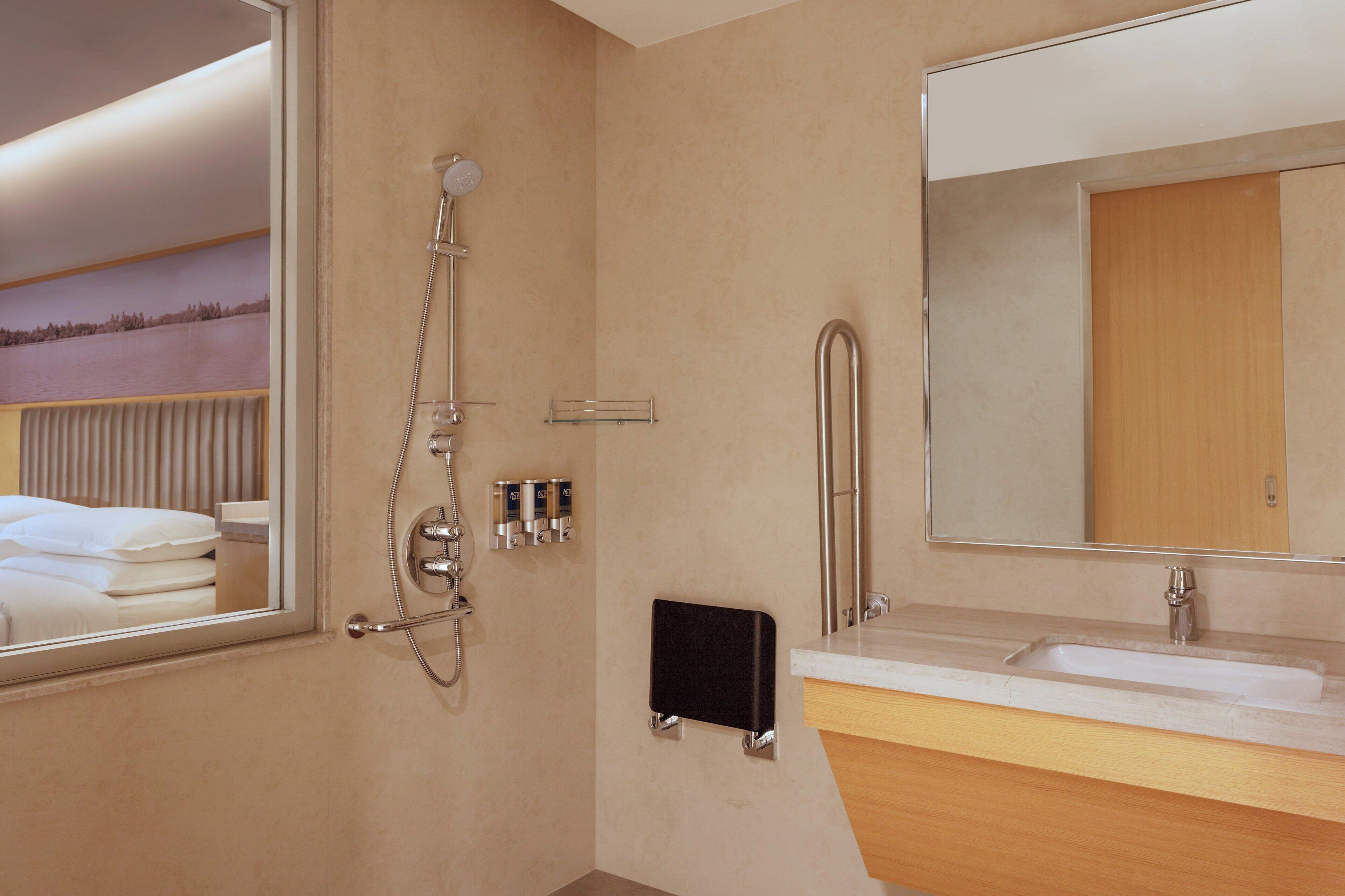 A modern bathroom with a large mirror, a shower, a sink, and a towel rack.