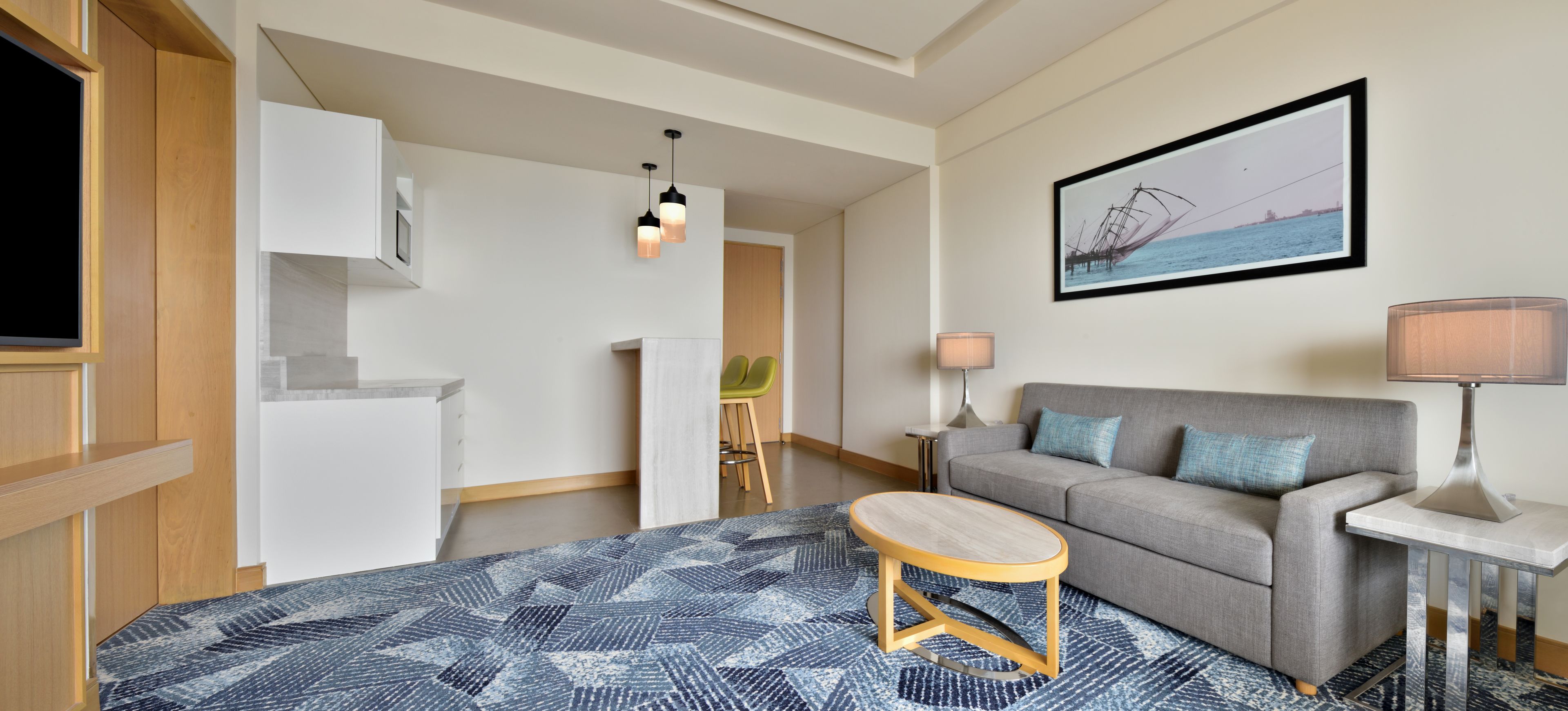 Una sala de estar moderna con un sofá gris, una mesa de centro redonda de madera, un tapete estampado y un cuadro en la pared.