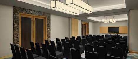 A conference room with rows of chairs, a large screen, and a stone accent wall.