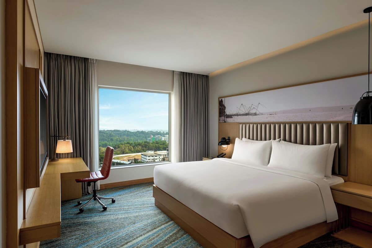 Une chambre d’hôtel avec un grand lit, un bureau avec une chaise, une table de chevet et une vue sur l’extérieur.