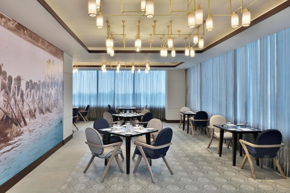 A modern dining area with round tables, chairs, and a large abstract mural on the wall.