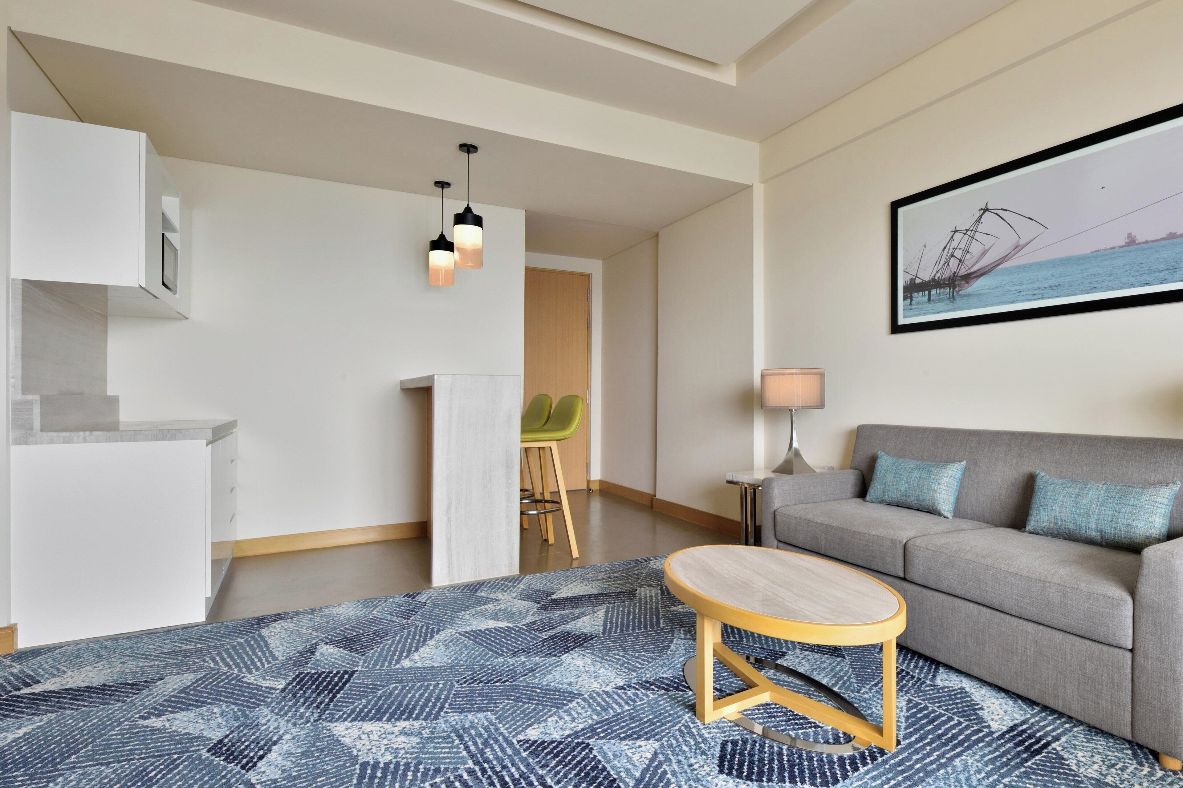 Een moderne woonkamer met een grijze bank, een ronde houten salontafel en een blauw gekleurd vloerkleed.
