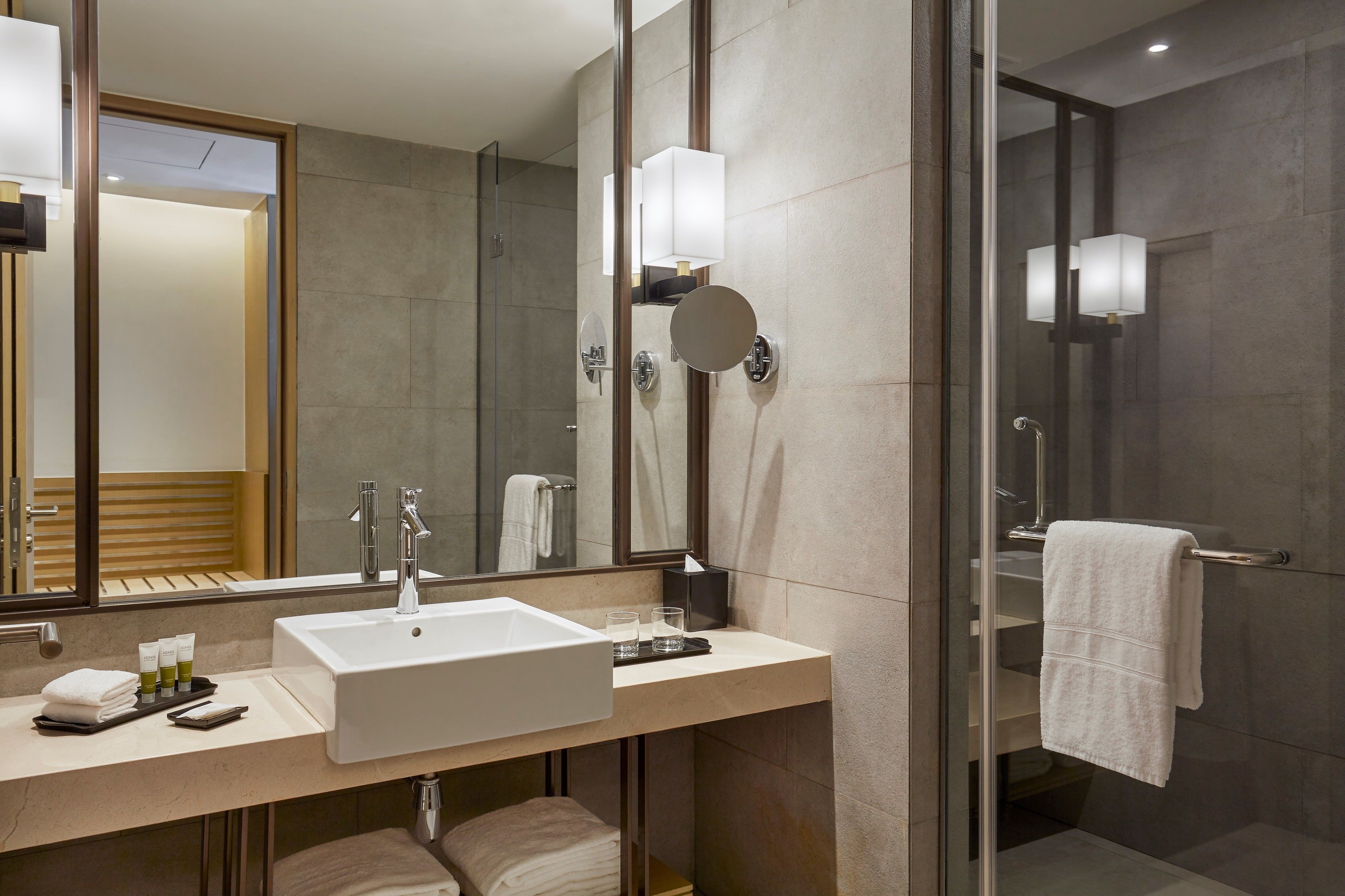 A modern bathroom with a large mirror, a sink, and a glass-enclosed shower.