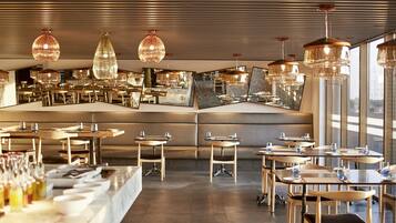 Ein modernes Restaurant mit mehreren Esstischen, gepolsterten Sitzgelegenheiten und großen Fenstern, die einen Ausblick bieten.