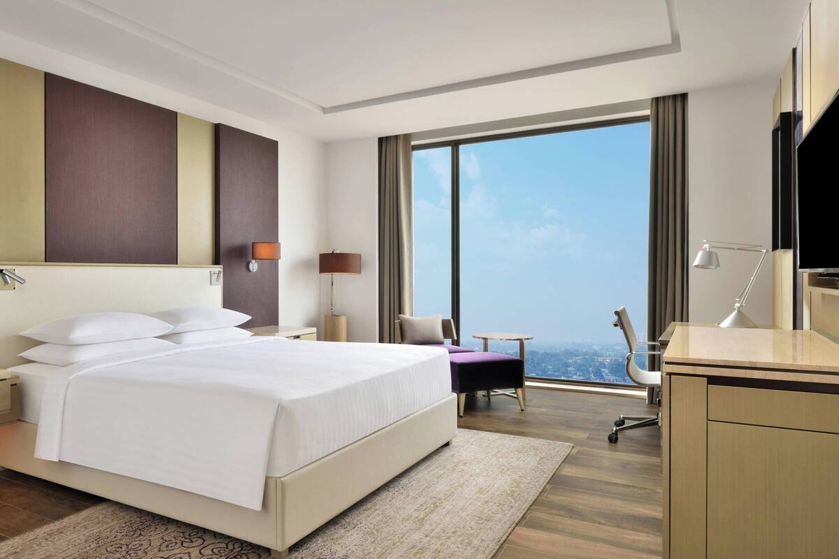 A hotel room with a large bed, a desk, a chair, a TV, and a view of the city.