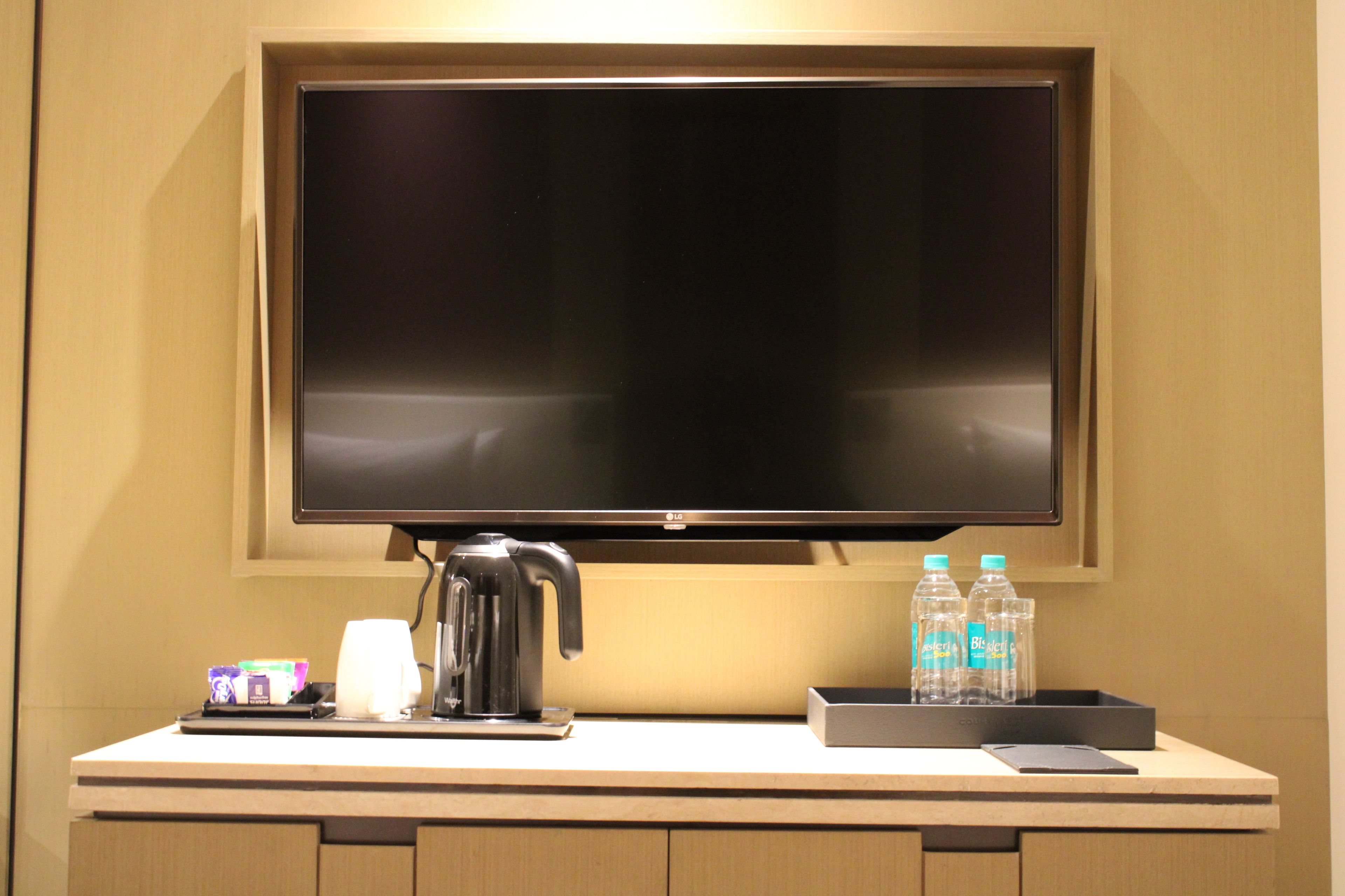 A hotel room with a flat-screen TV mounted above a counter, a coffee maker, and two water bottles on the counter.