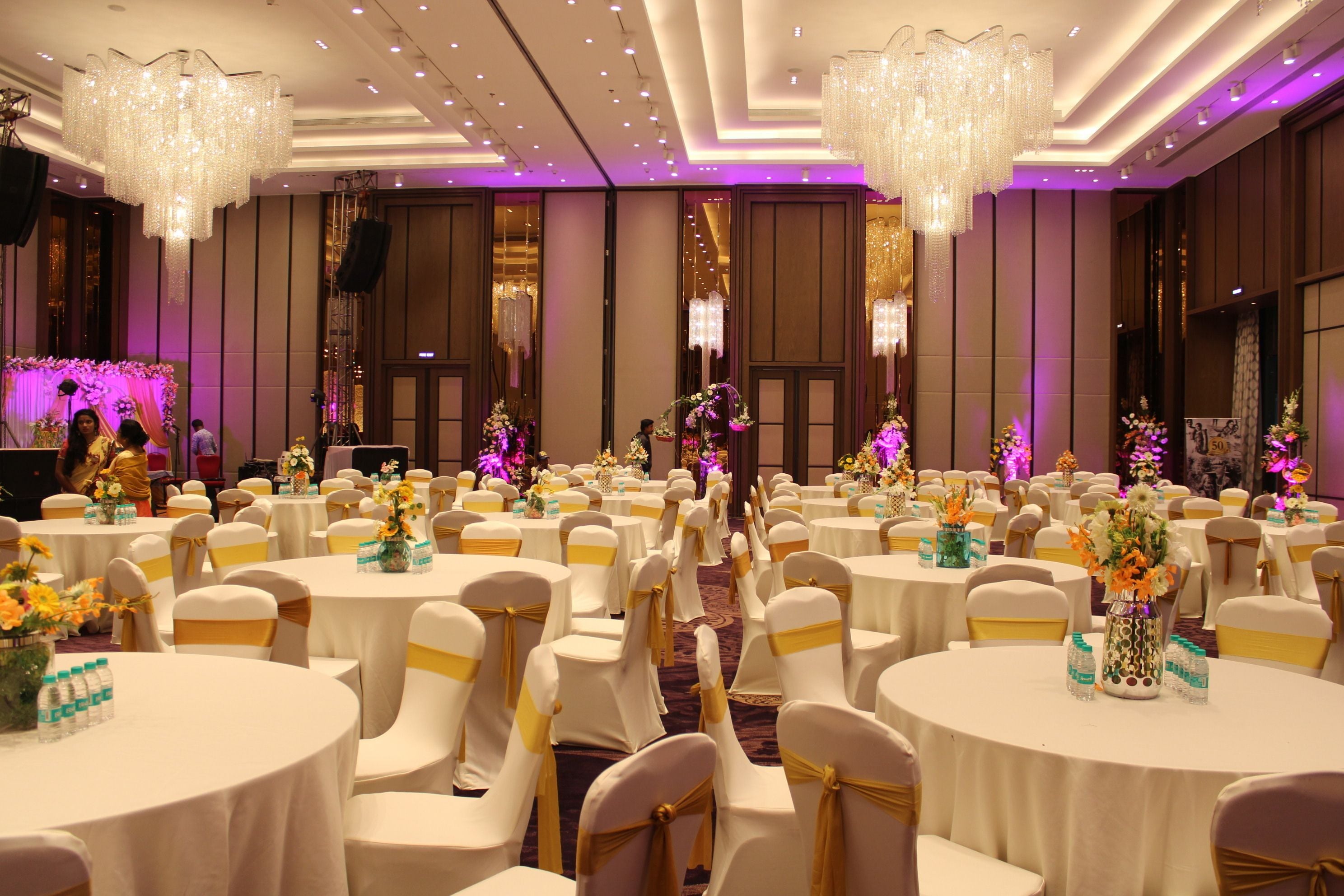 A banquet hall with round tables, chairs, and chandeliers.