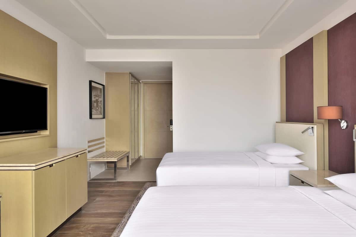 A hotel room with two beds, a television, a desk, and a bathroom visible through an open door.